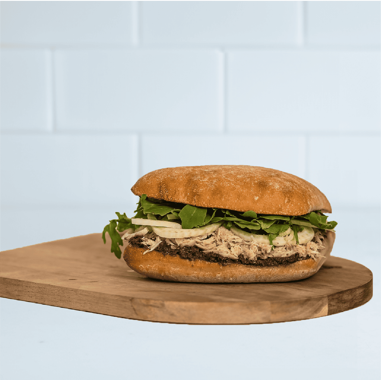 A Root & Sprig signature Tuna Sandwich on a wooden charcuterie board. 